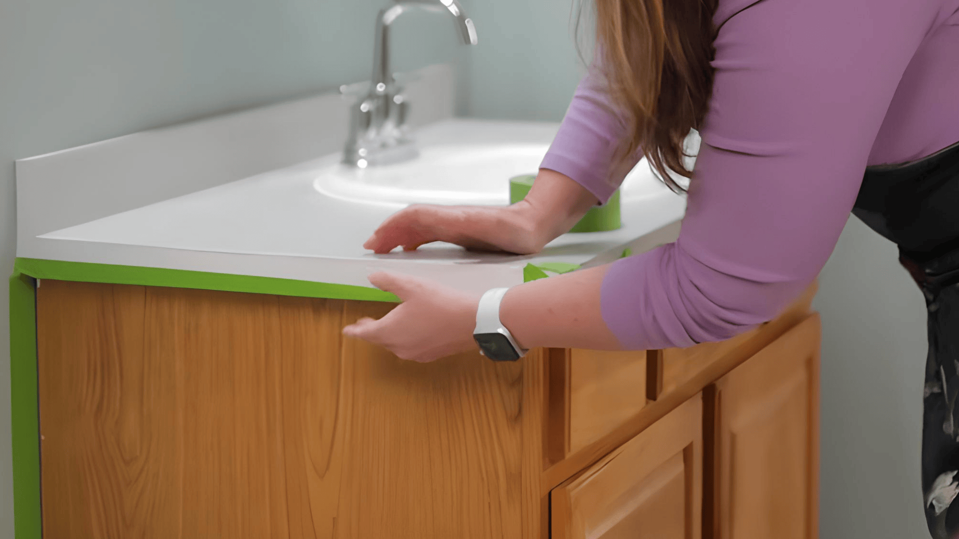 a person wipes a wooden cabinet with sandpaper beneath a bathroom sink counter smoothing the surface before finishing (1)