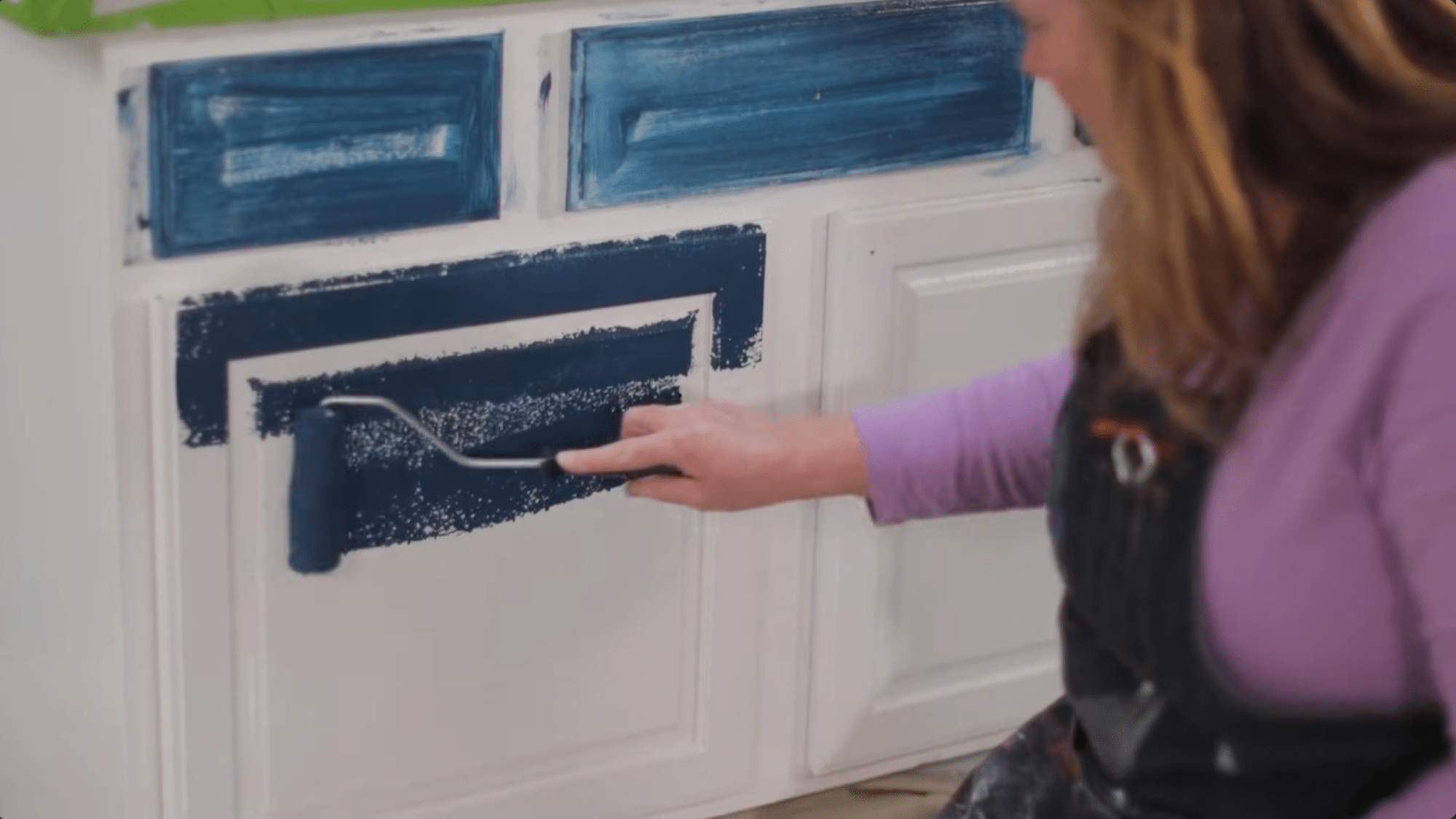 applying dark paint with a roller while painting bathroom cabinets for smooth even coverage on cabinet doors