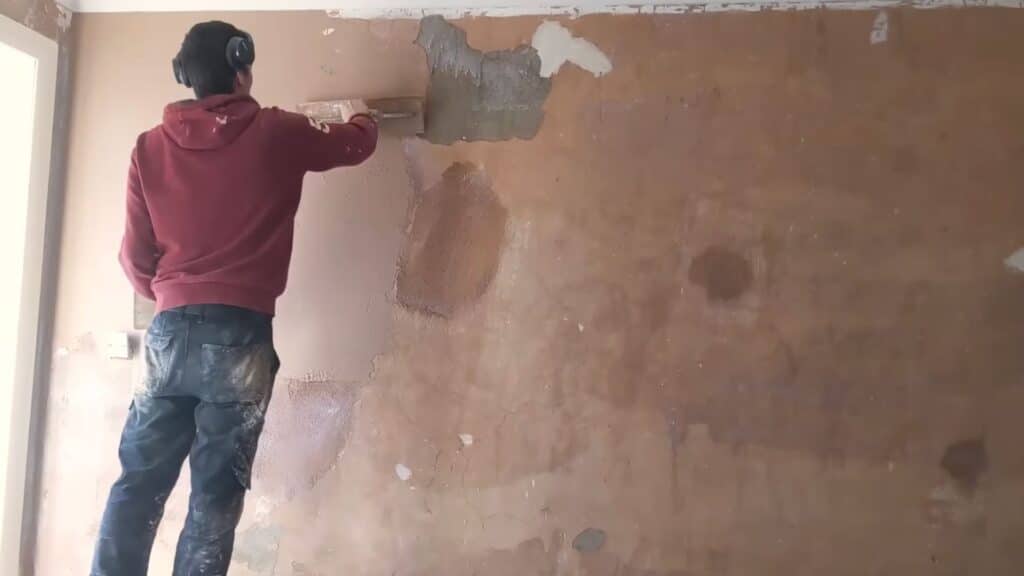 applying first coat of plaster on wall with trowel spreading base layer evenly across surface