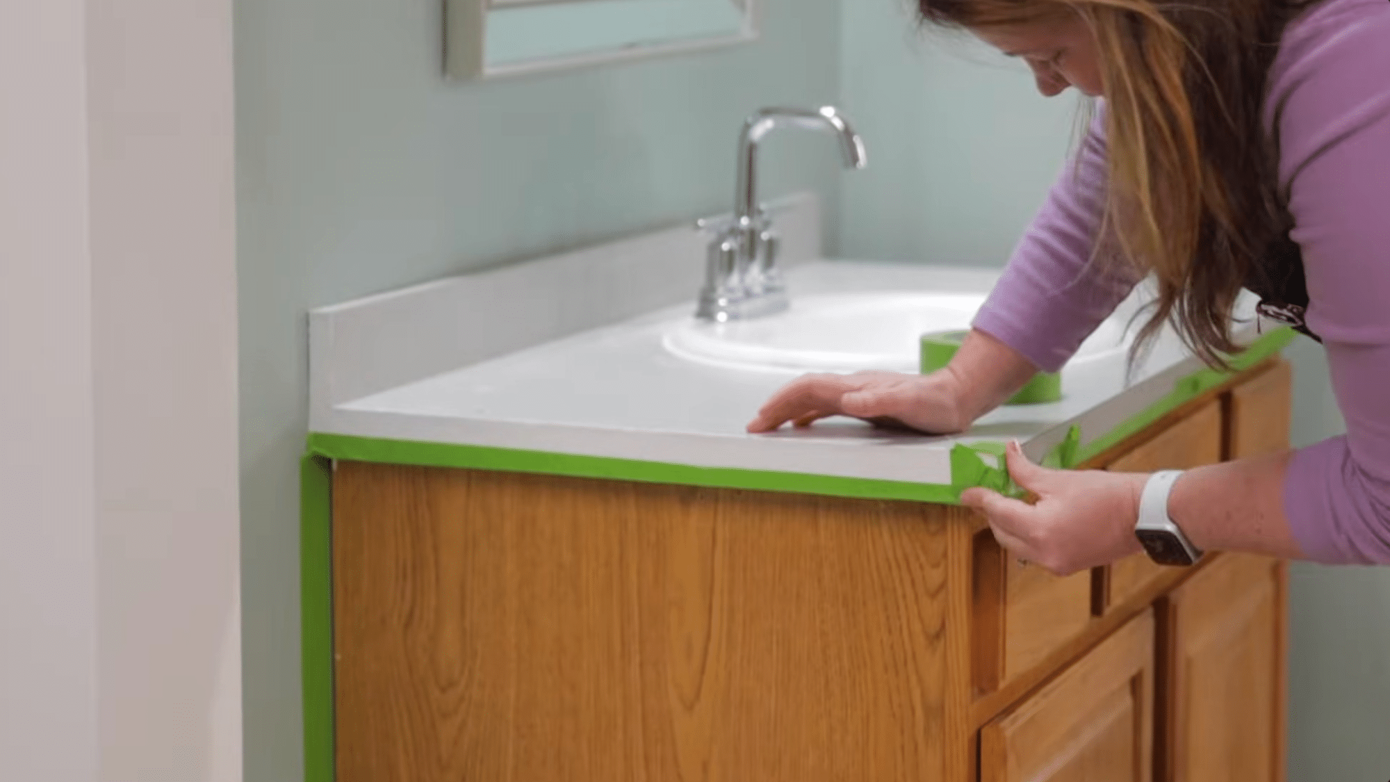 applying painter tape around vanity edges before painting bathroom cabinets to protect walls and surfaces