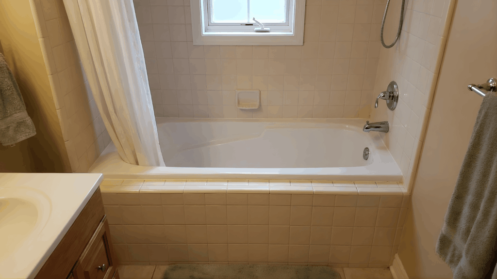 bathroom with tiled alcove bathtub shower combo under window with curtain chrome fixtures and towel hanging on wall
