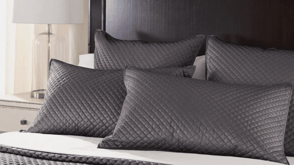 bed with beige quilted pillow shams layered on white bedding against dark headboard