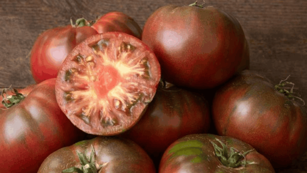 black krim tomatoes with dark red color whole and sliced showing inside texture on wooden surface