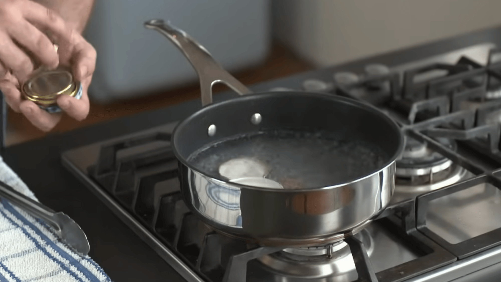 boiling water in pan with jar lids inside heating to clean and prepare lids for safe sealing process