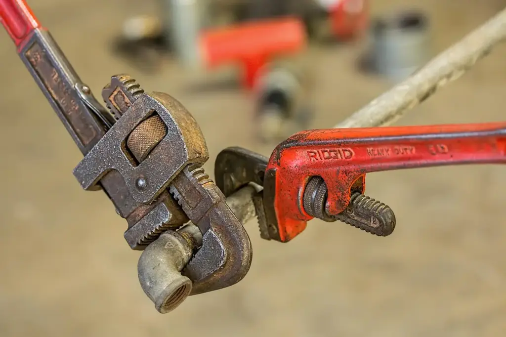 Two pipe wrenches gripping a metal pipe in a workshop setting