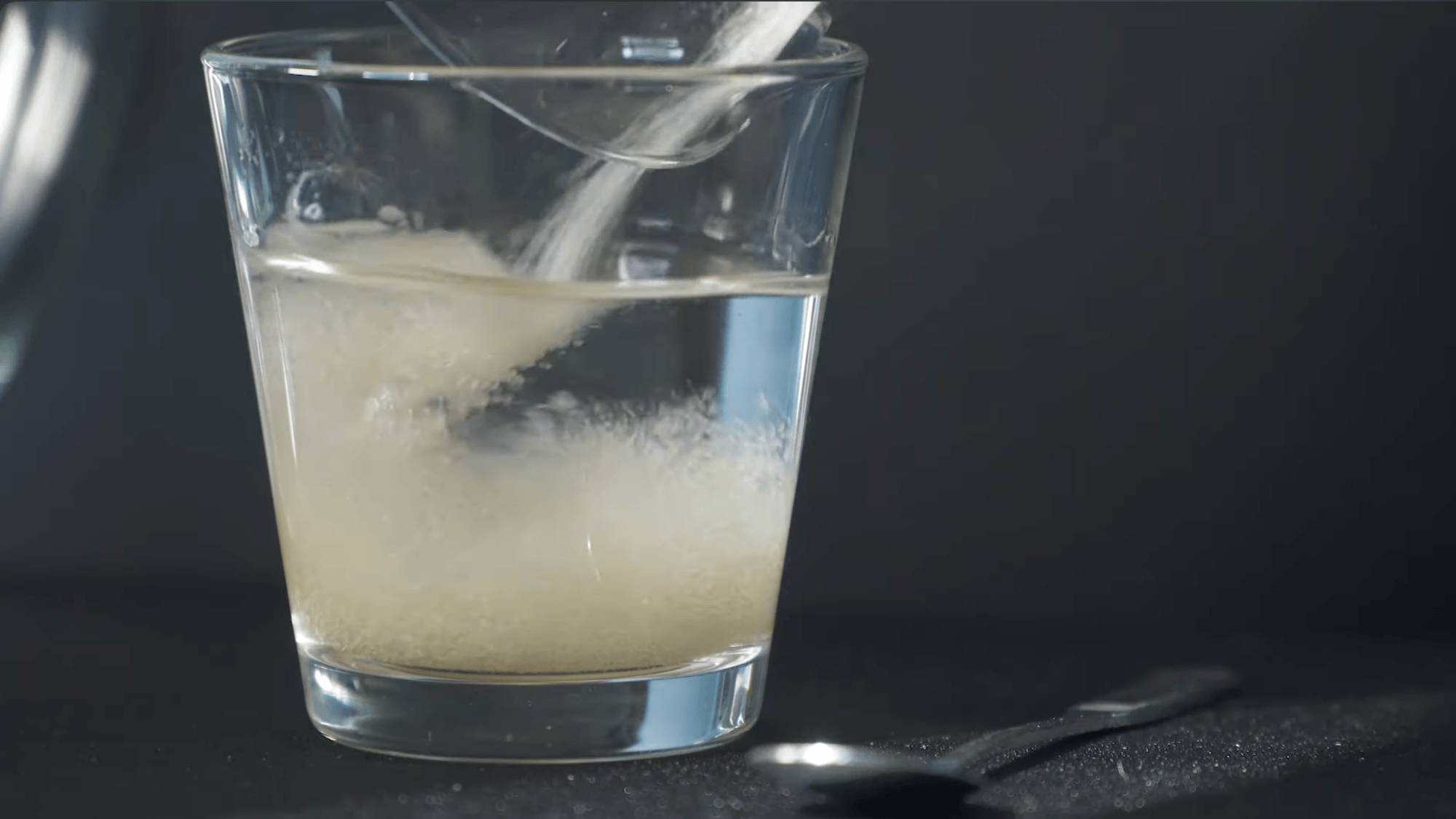 glass of water with white powder being poured and dissolving creating cloudy mixture on dark surface