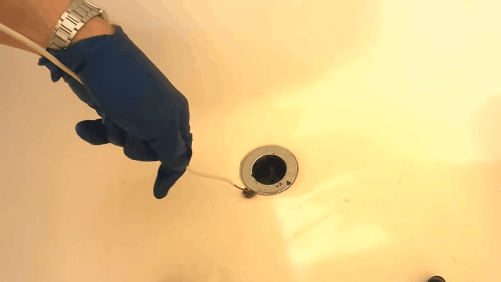 gloved hand pulling hair clog from bathtub drain demonstrating how to unclog a bathtub drain