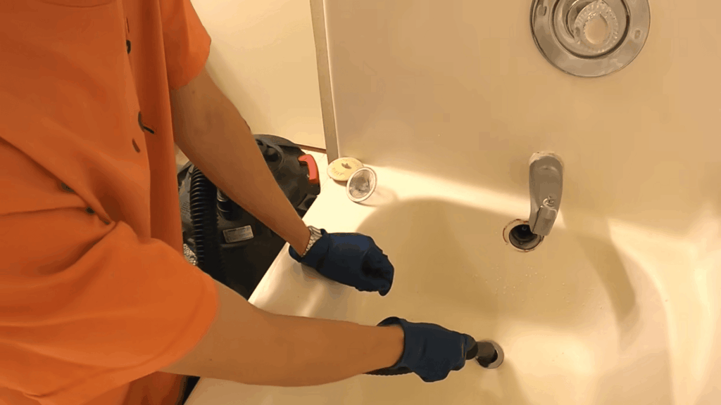 gloved hands using drain tool in bathtub showing how to unclog a bathtub drain with simple cleaning method