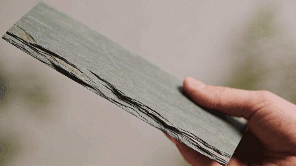 hand holding thin layered slate rock showing texture and edges demonstrating what type of rock is slate