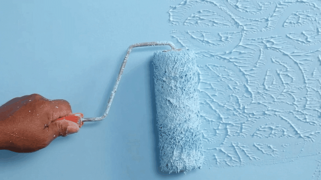 hand using paint roller to create textured wall pattern with raised swirls on blue surface showing wall texture technique