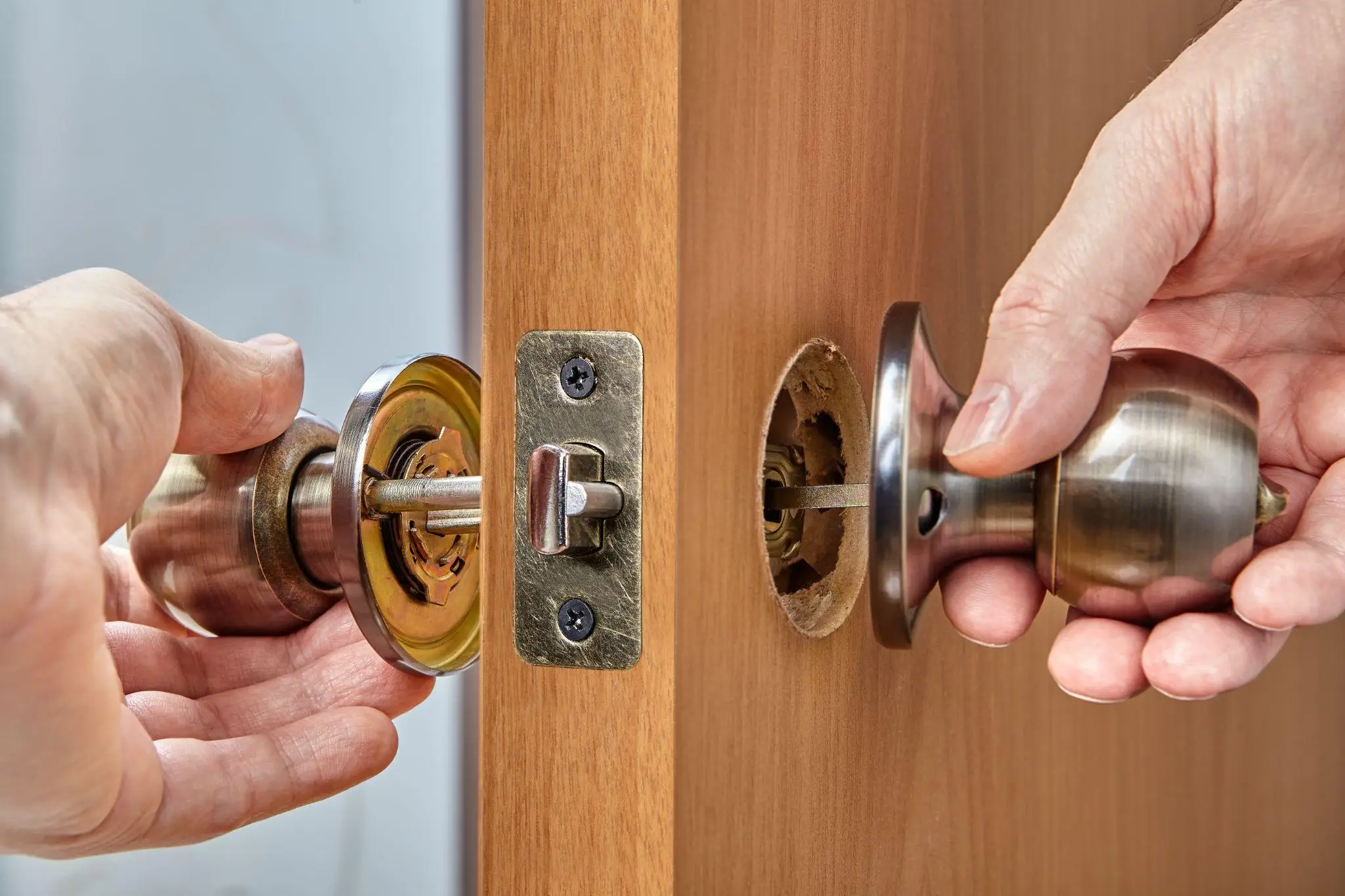 Hands installing a metallic door knob on a wooden door