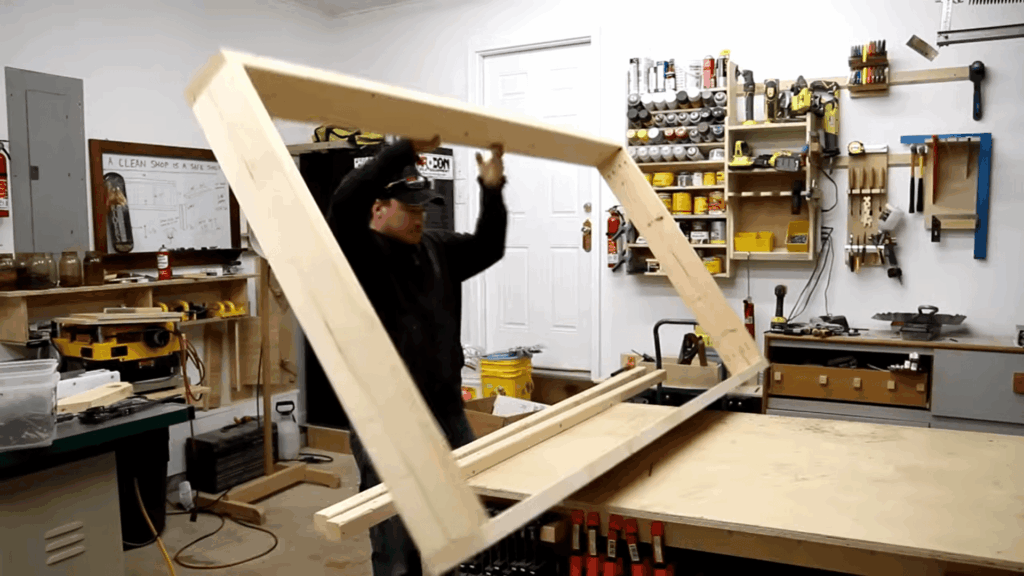 man lifting wooden frame in workshop assembling diy bunk beds with tools and lumber on workbench