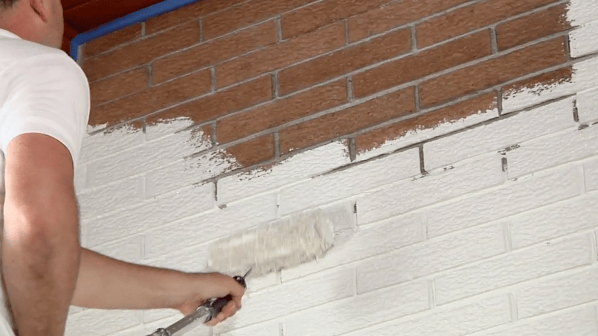 man painting brick wall with roller and filling gaps with a brush