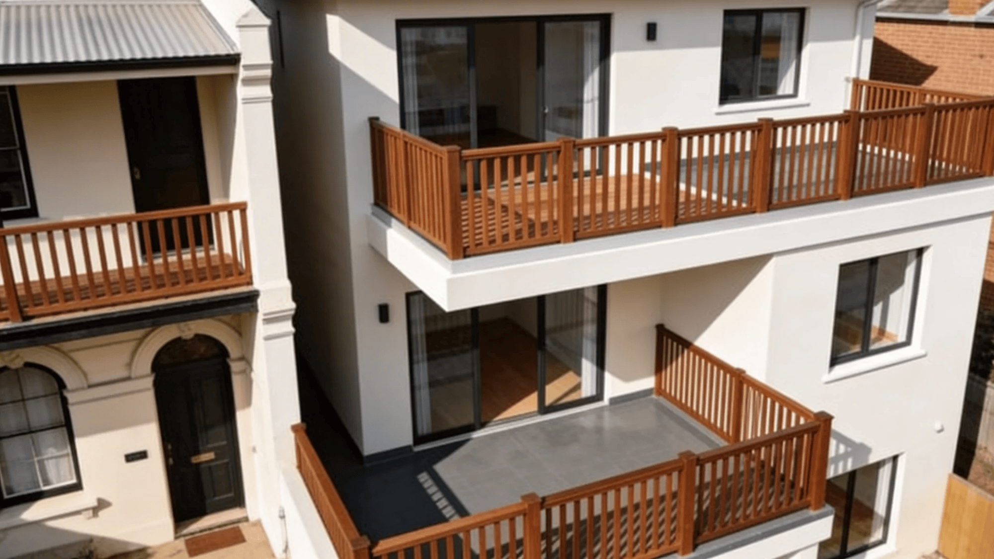 modern house exterior with multiple balconies wooden railings and large glass doors in daylight