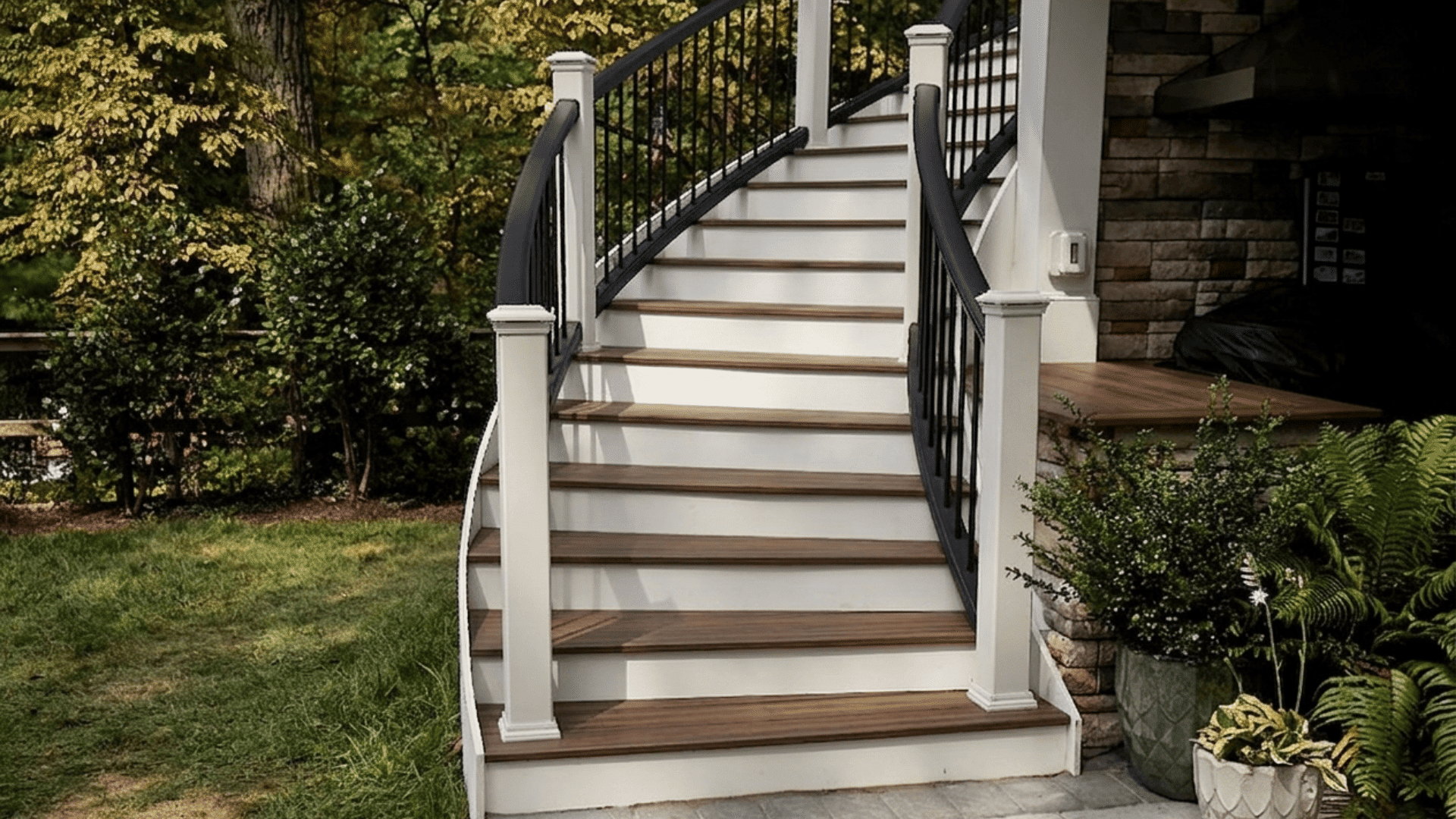 outdoor wooden stairs with white risers black railing and curved design leading to a porch surrounded by plants and trees