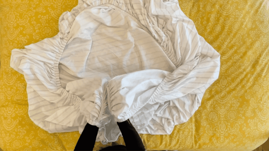 overhead view of fitted sheet spread on bed showing joining the two corner with elastic edges on yellow bedding