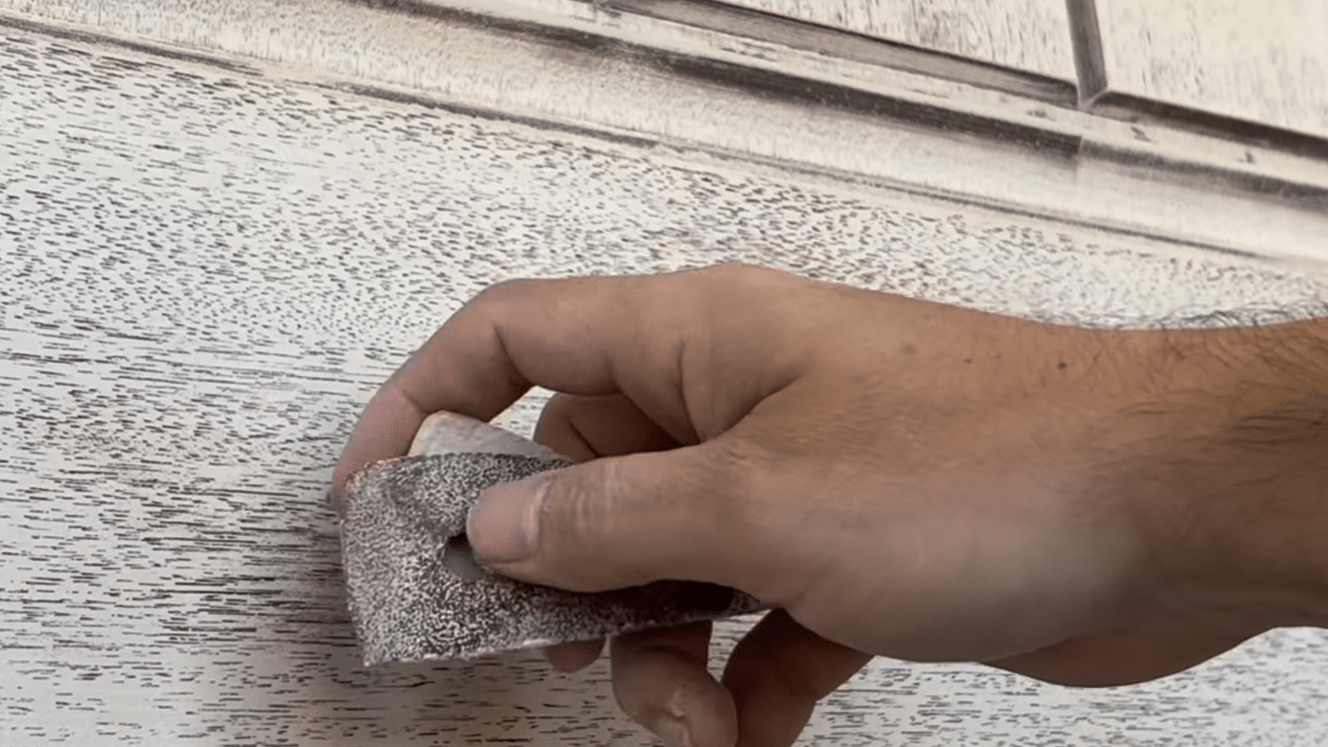 painting front door black preparation showing hand using sanding sponge on primed door surface before painting exterior door