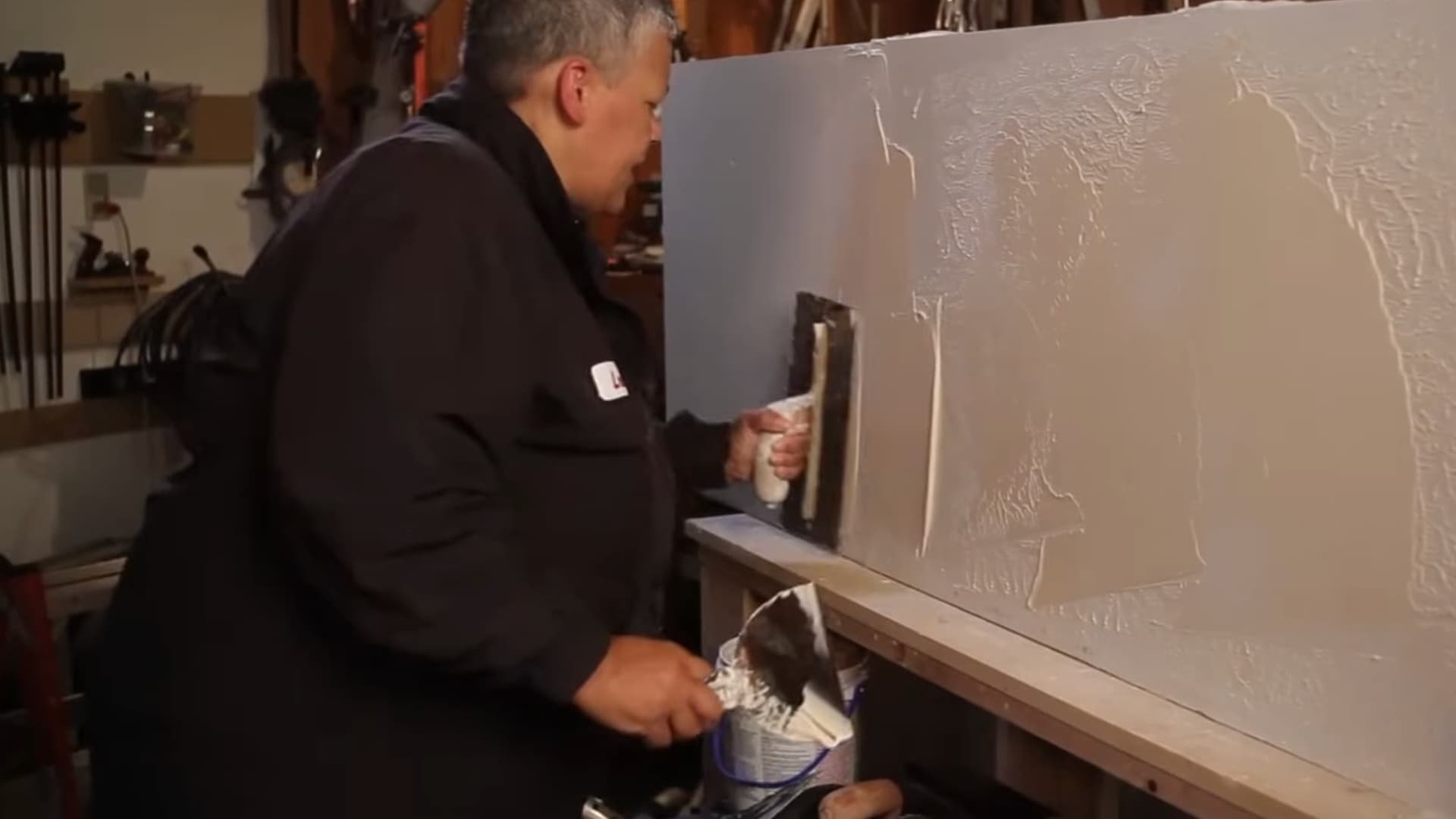 person applying plaster with trowel on panel demonstrating textured wall creation technique during interior wall finishing process