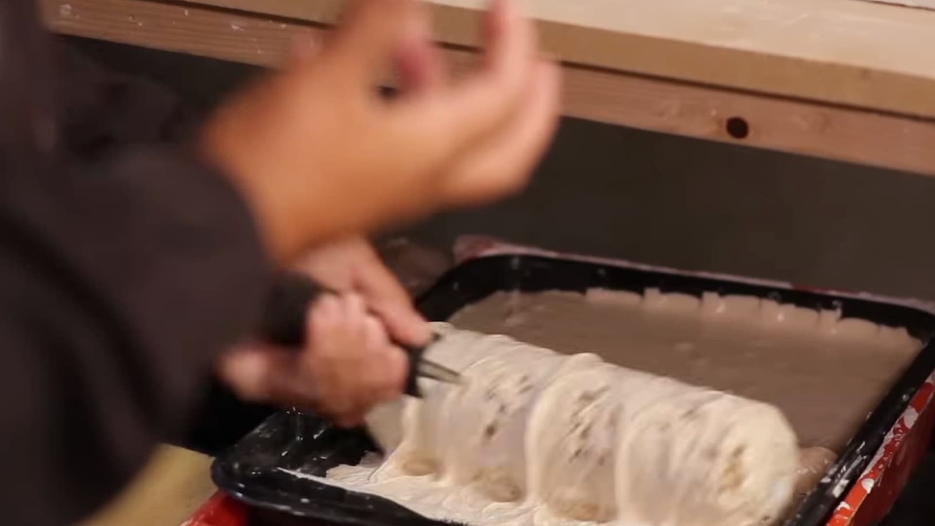 person rolling thick plaster mixture in paint tray preparing surface for textured wall finish during interior wall project