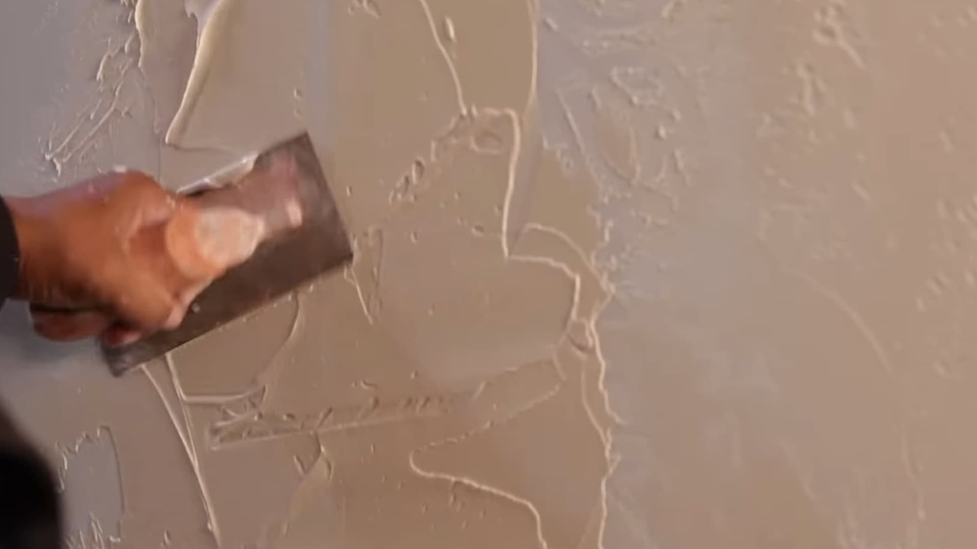 person spreading plaster with metal trowel on surface creating textured wall finish during interior wall finishing process