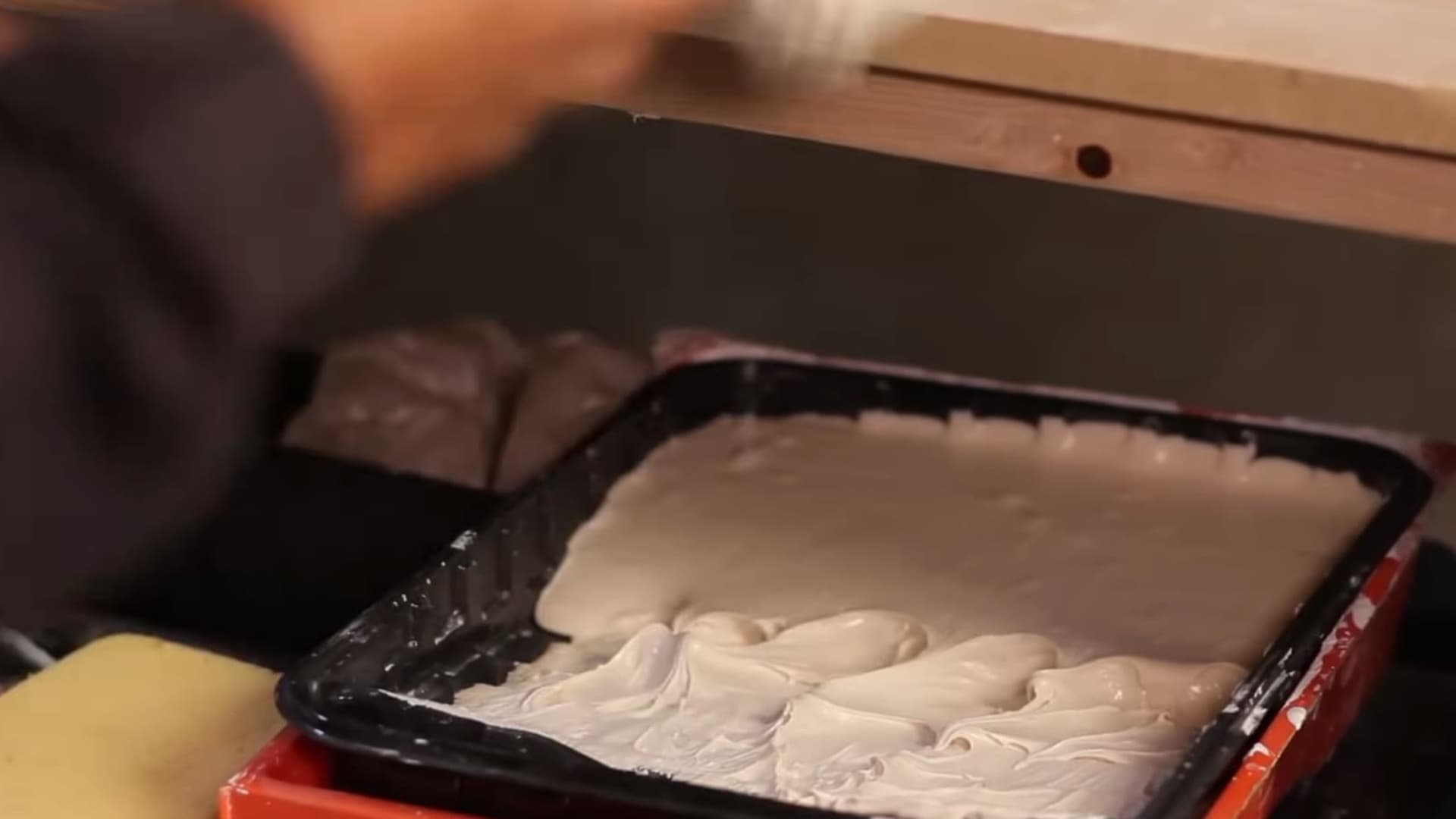 person spreading thick white plaster mixture in black tray while preparing surface for textured wall finishing indoors