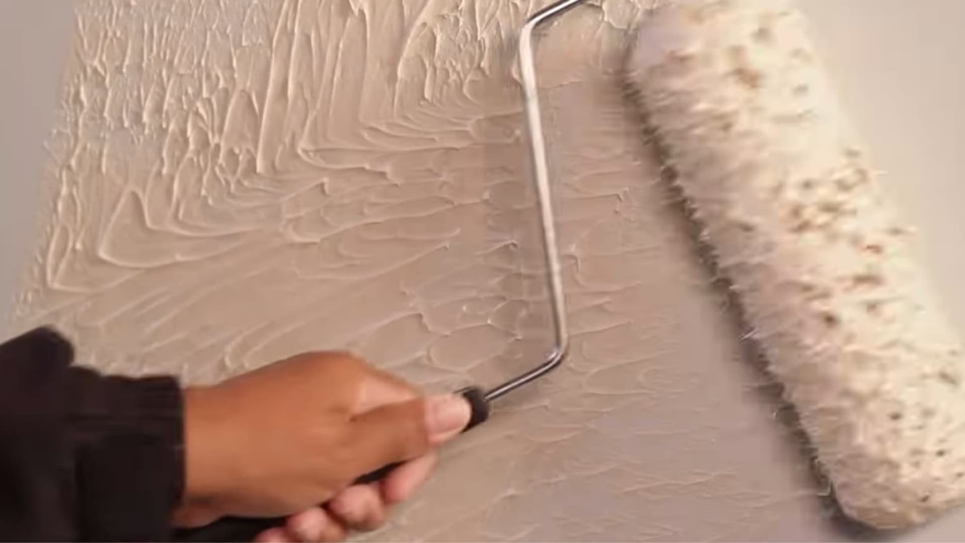 person using paint roller to apply plaster pattern creating textured wall finish during interior wall decoration process
