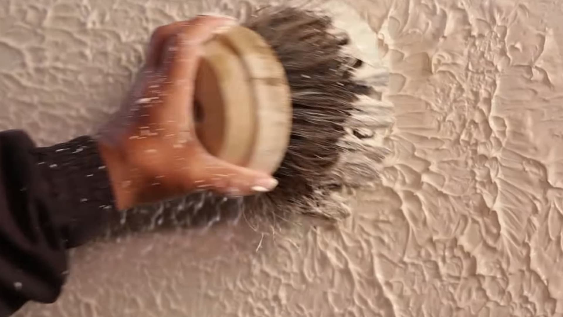 person using round brush to dab plaster creating decorative textured wall pattern during interior wall finishing process
