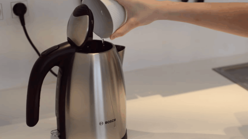 pouring vinegar and water solution into electric kettle for cleaning step two process