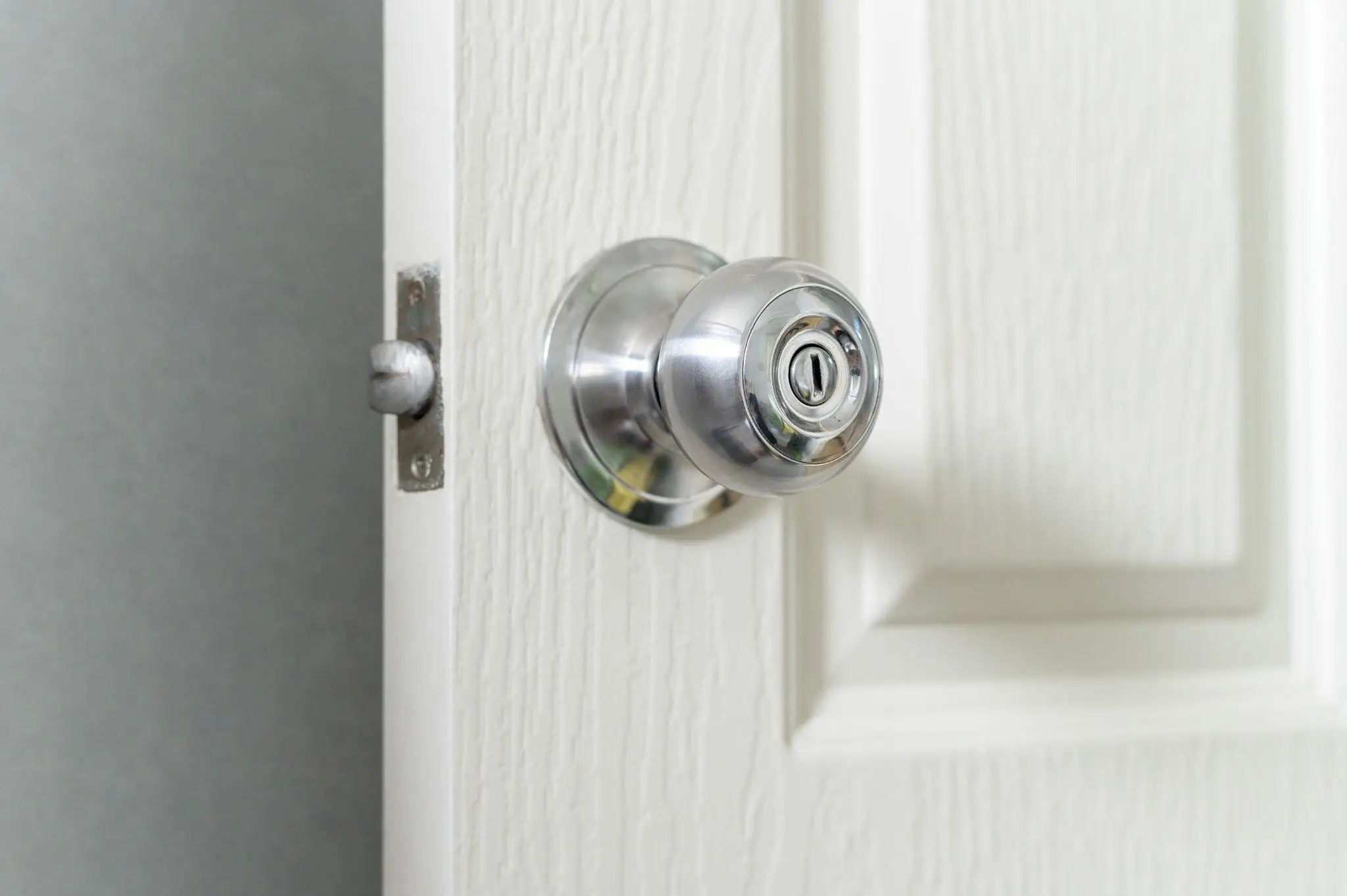 Close-up of a brushed metal doorknob on a partially open white door