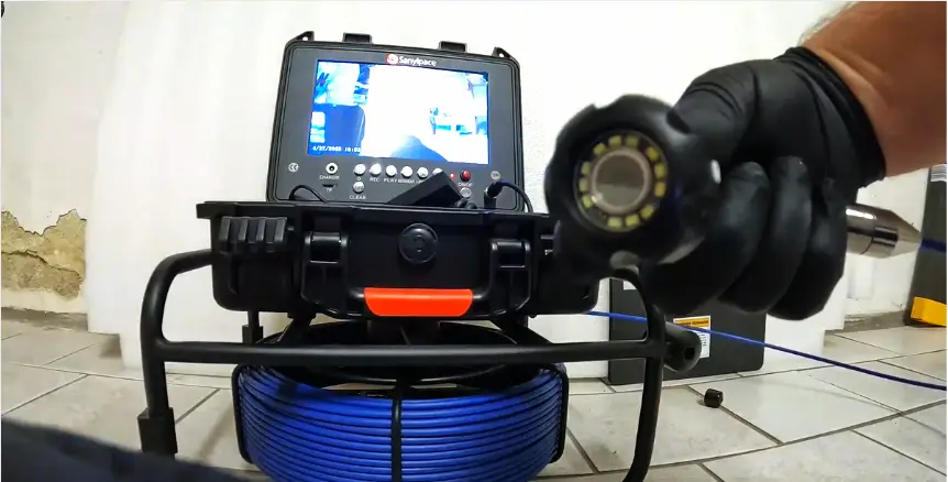 Plumber using inspection camera with monitor and blue cable in tiled room