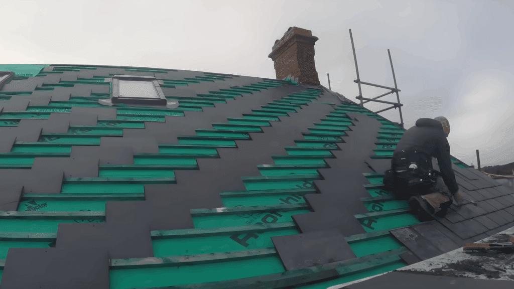 slate roof installation in progress with a worker adding tiles to the roof using a hammer and precision tools