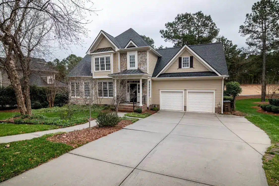 Two-story suburban house with gabled roof, in front of a wide concrete driveway