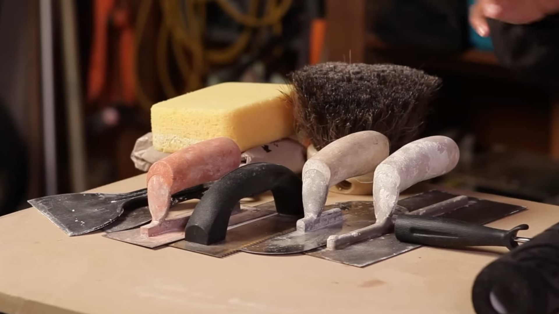 tools and brushes used to create textured wall finish including trowels sponge and brush arranged on workbench for wall plastering process
