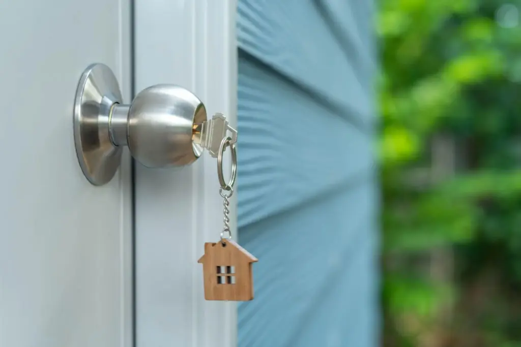 Upgrading Your Home Security With Knob Locksets Key in silver door knob with house-shaped keychain on blue siding door