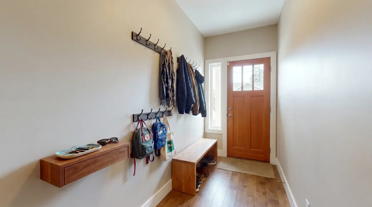 Wall hooks with coats and bags above a small tray in a narrow entryway