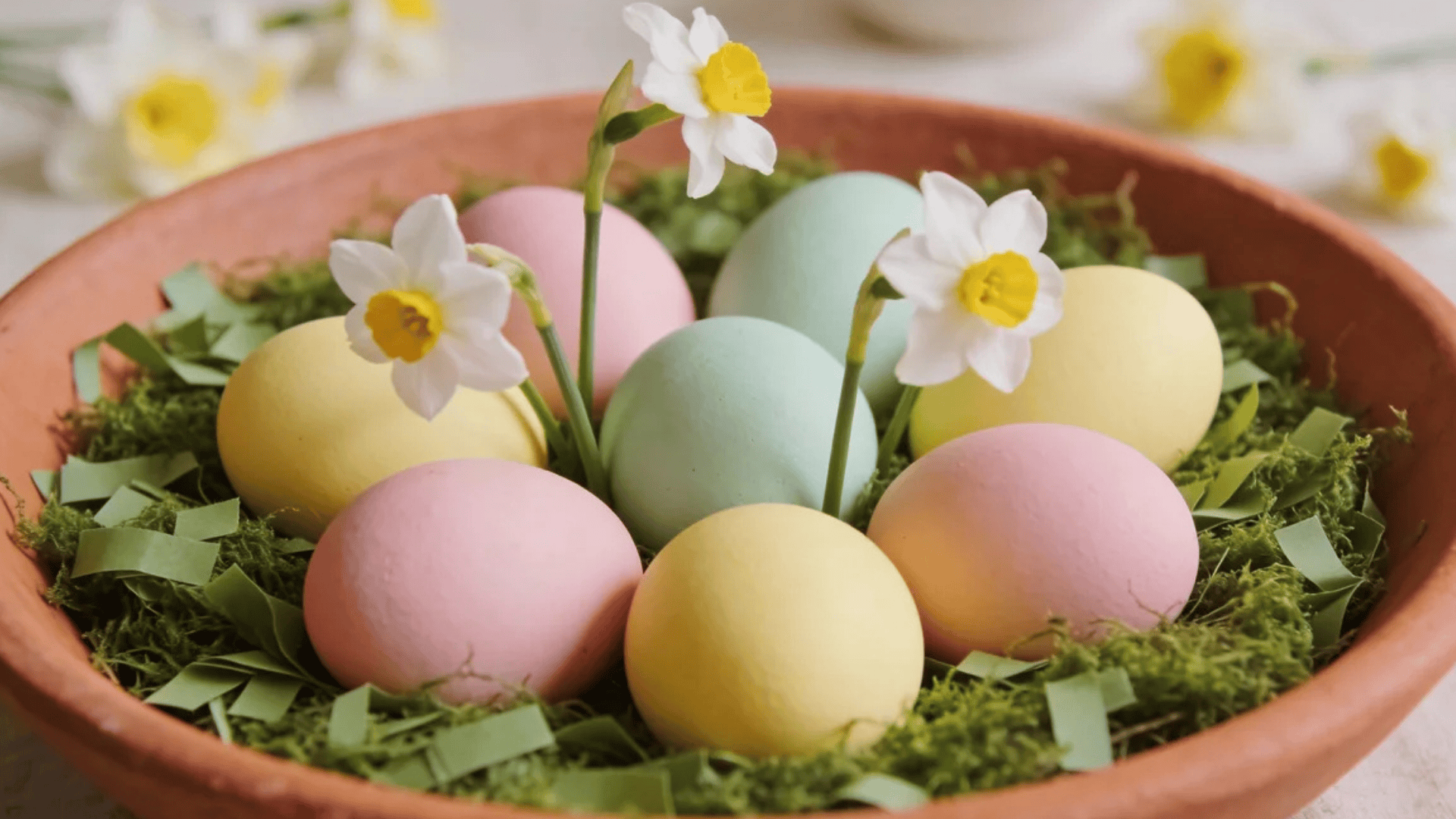a bowl with pastel colored eggs and small flowers arranged in green moss creating a soft spring display
