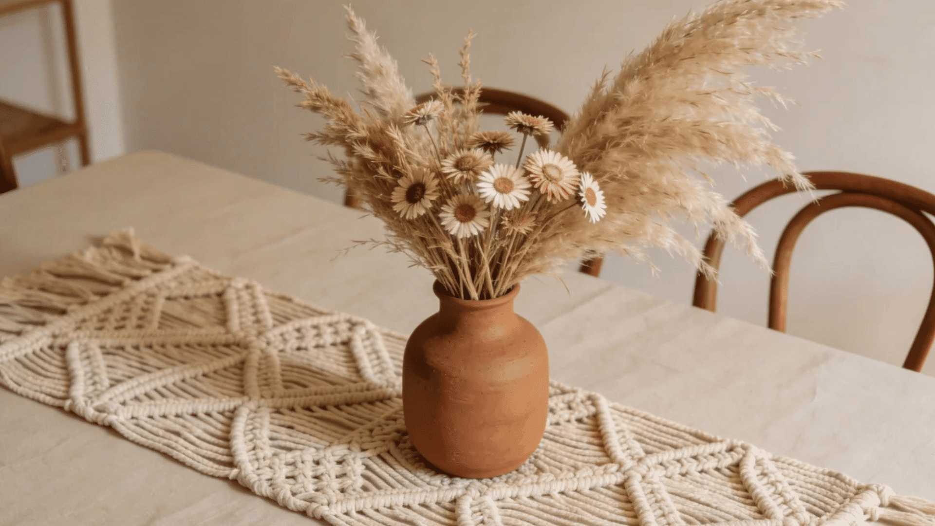 a ceramic vase with dried flowers on table with woven runner in neutral room with soft light