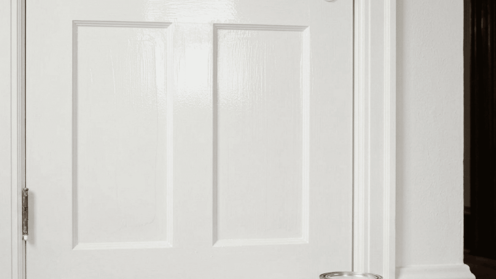 a freshly painted white door with brushes roller and paint can placed on floor showing completed painting work