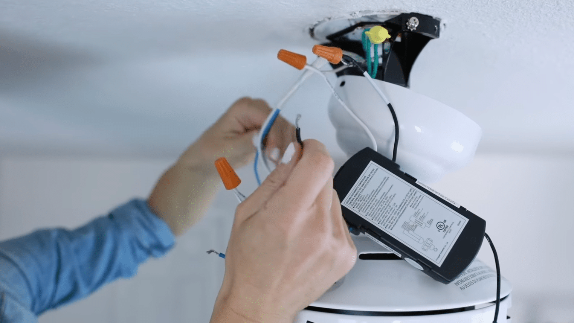 a person connecting ceiling fan wires and remote receiver while installing electrical components on a ceiling mount