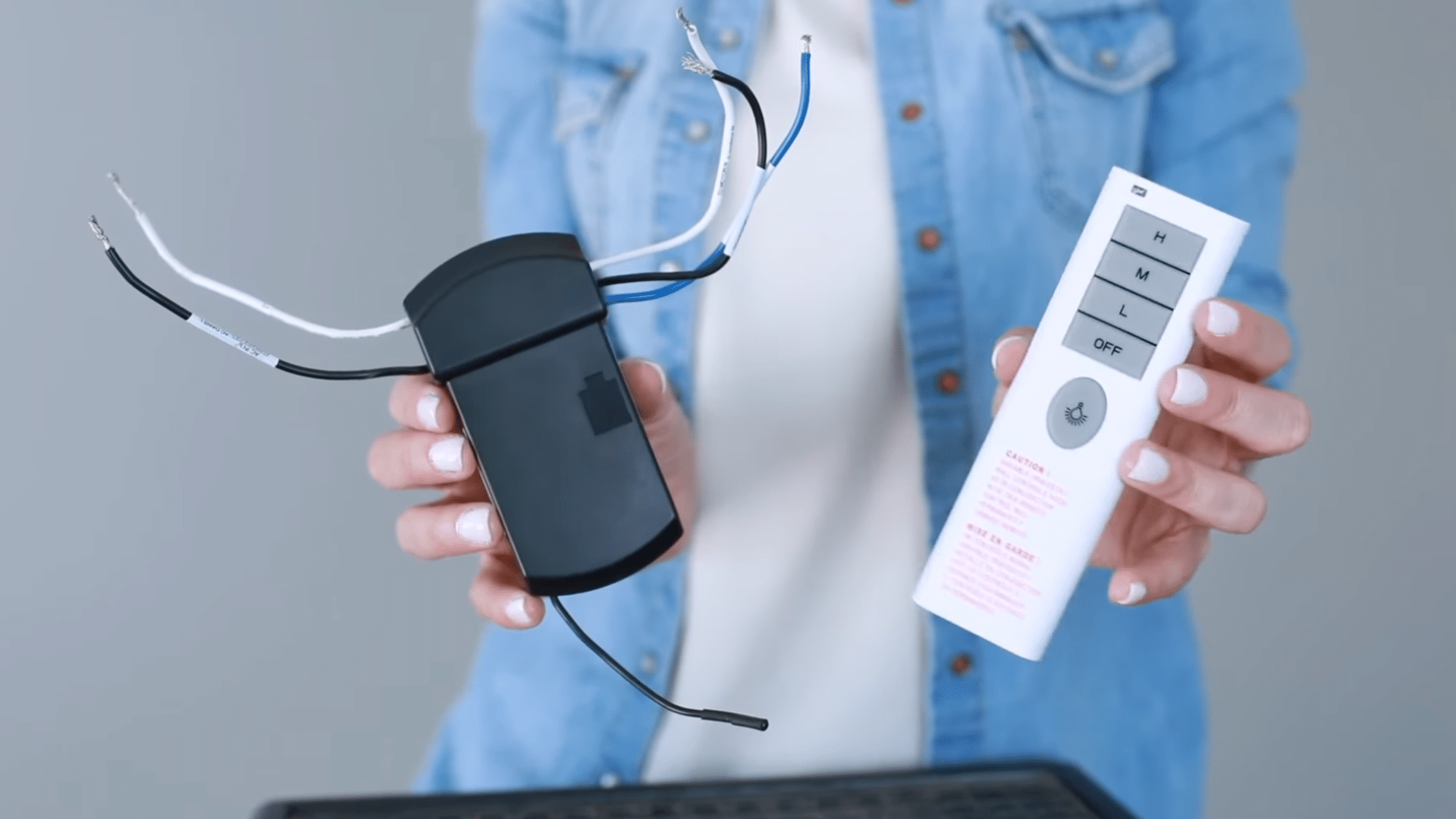 a person holding a ceiling fan remote and wiring receiver with exposed wires for electrical installation setup