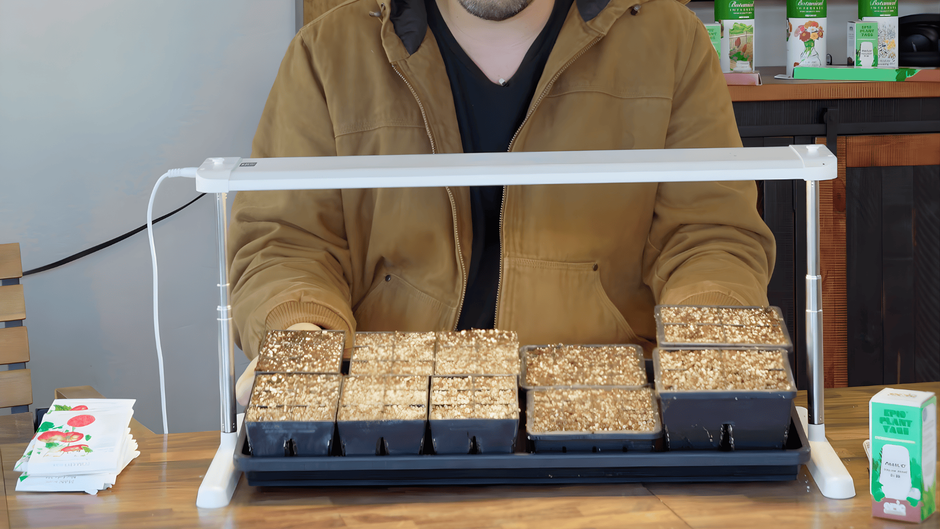 a person setting up seed trays under grow light on table how to start seeds indoors