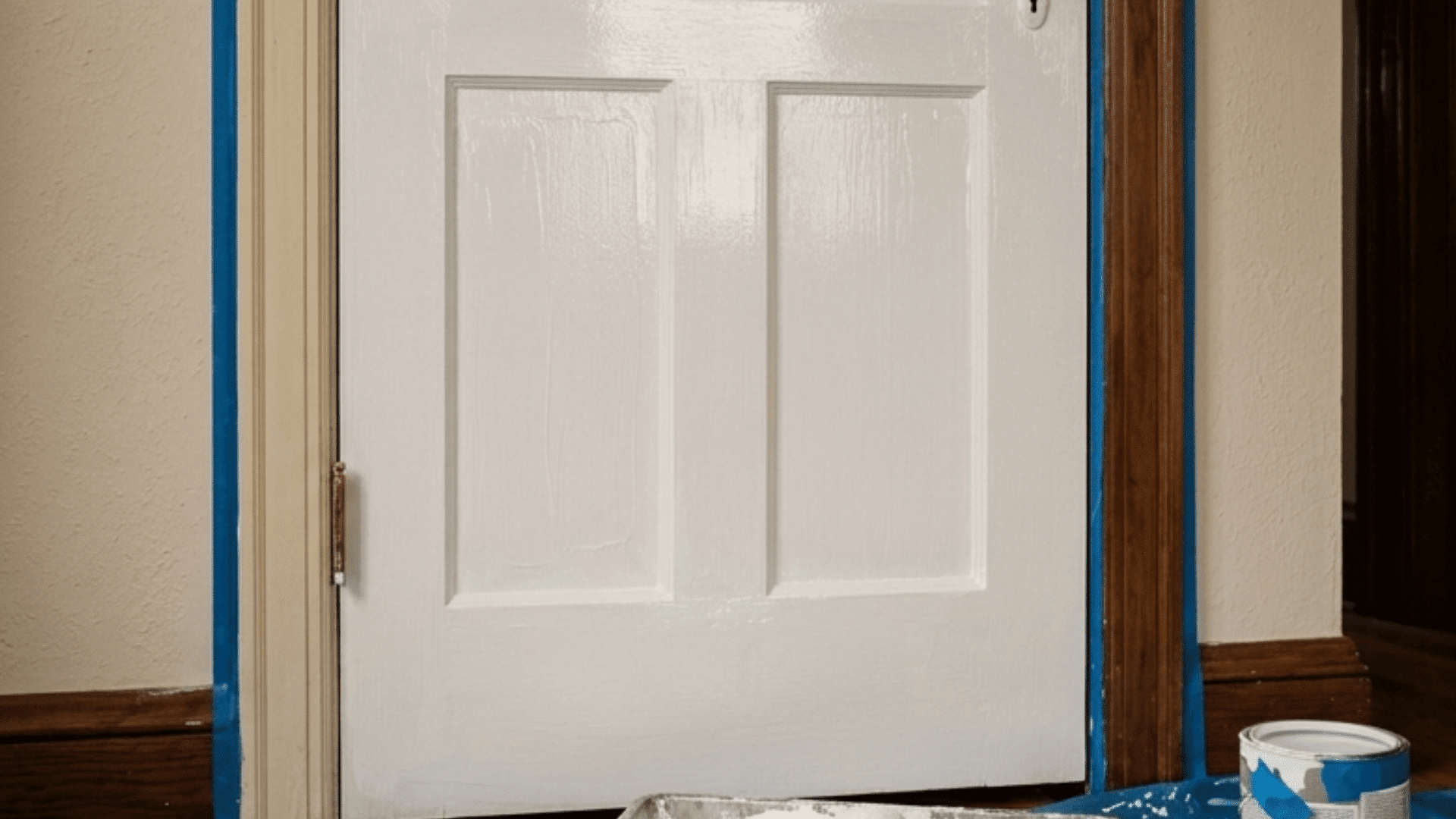 a wooden door being painted white with roller tray tools and protective sheet on floor
