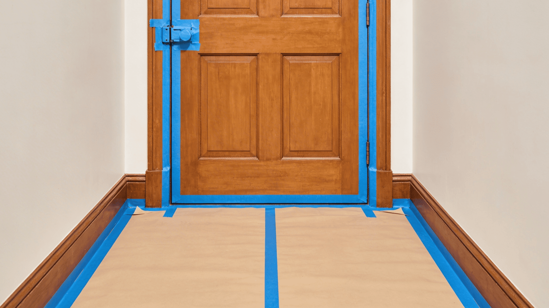 a wooden door masked with blue tape and paper on floor preparing for painting in a hallway setting