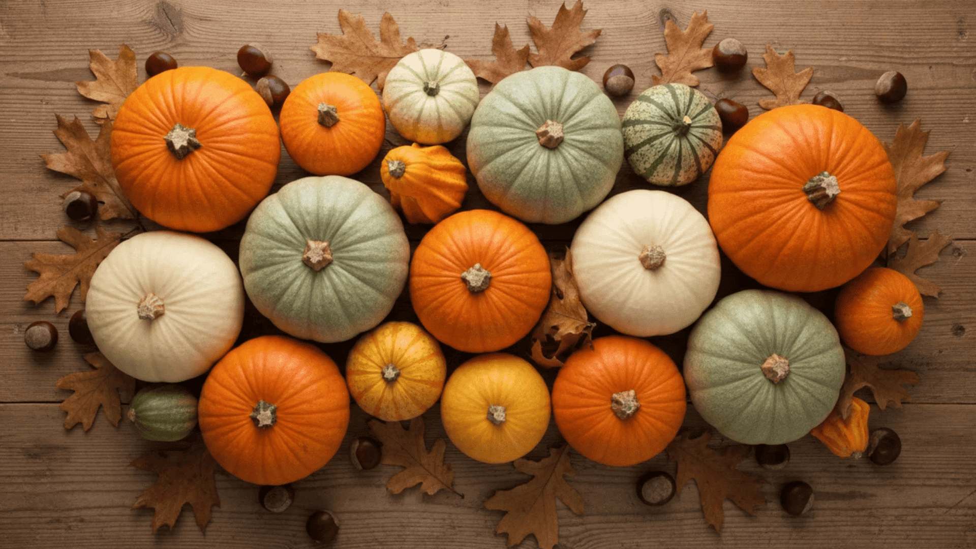 an arrangement of colorful pumpkins on wooden surface with autumn leaves and chestnuts creating seasonal display (1)