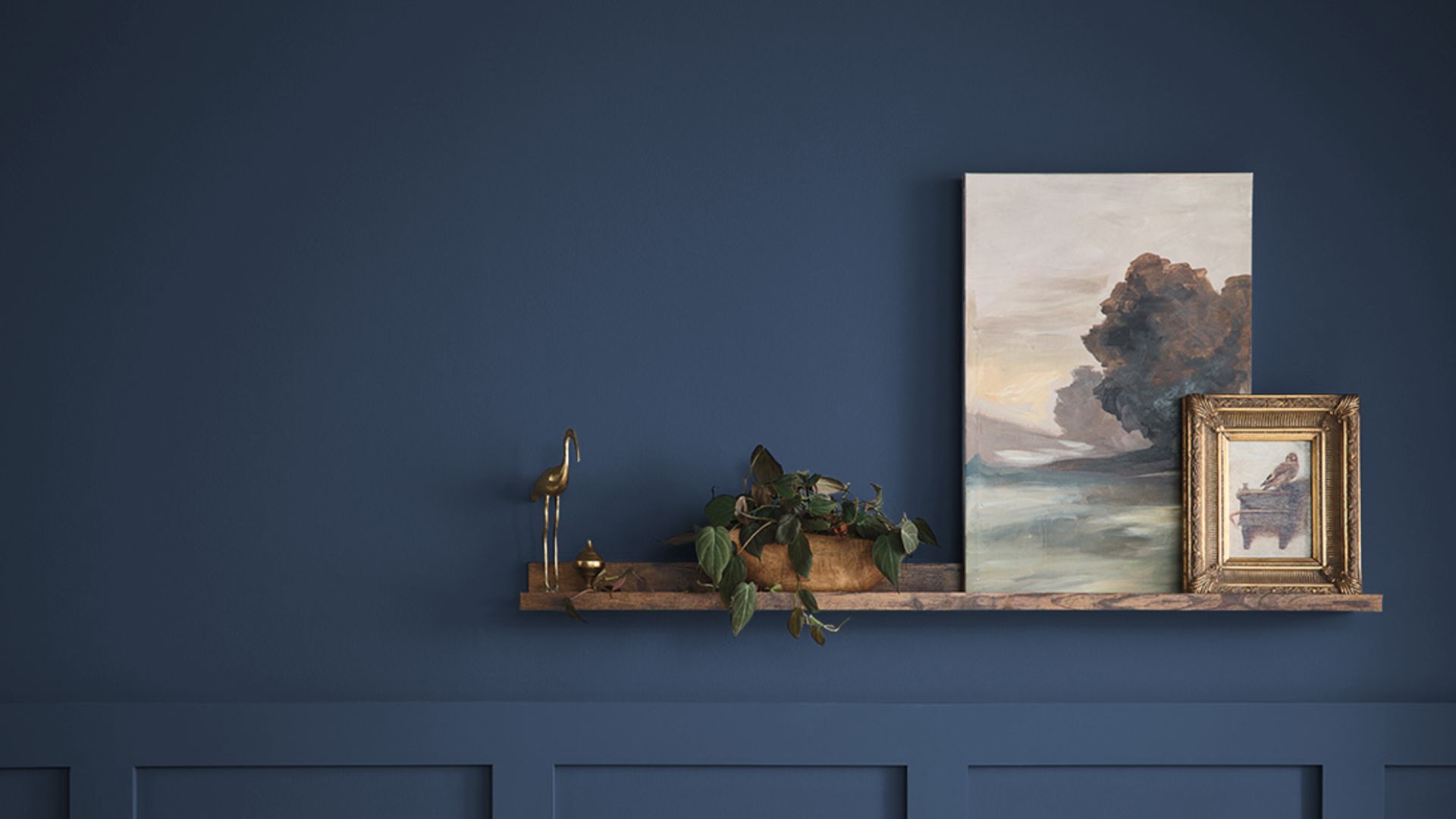 blue wall with wooden shelf holding framed artwork small plant and decorative objects arranged neatly against paneled wall