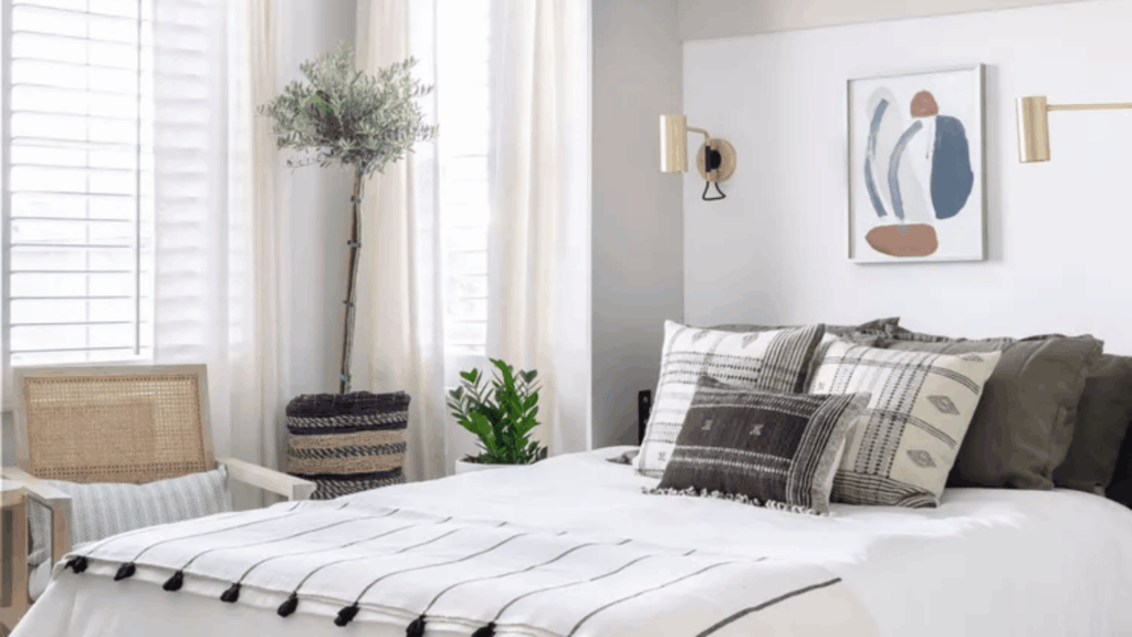 bright cozy bedroom with white bed layered pillows wall art plants and chair near window showing simple spare bedroom ideas for guests