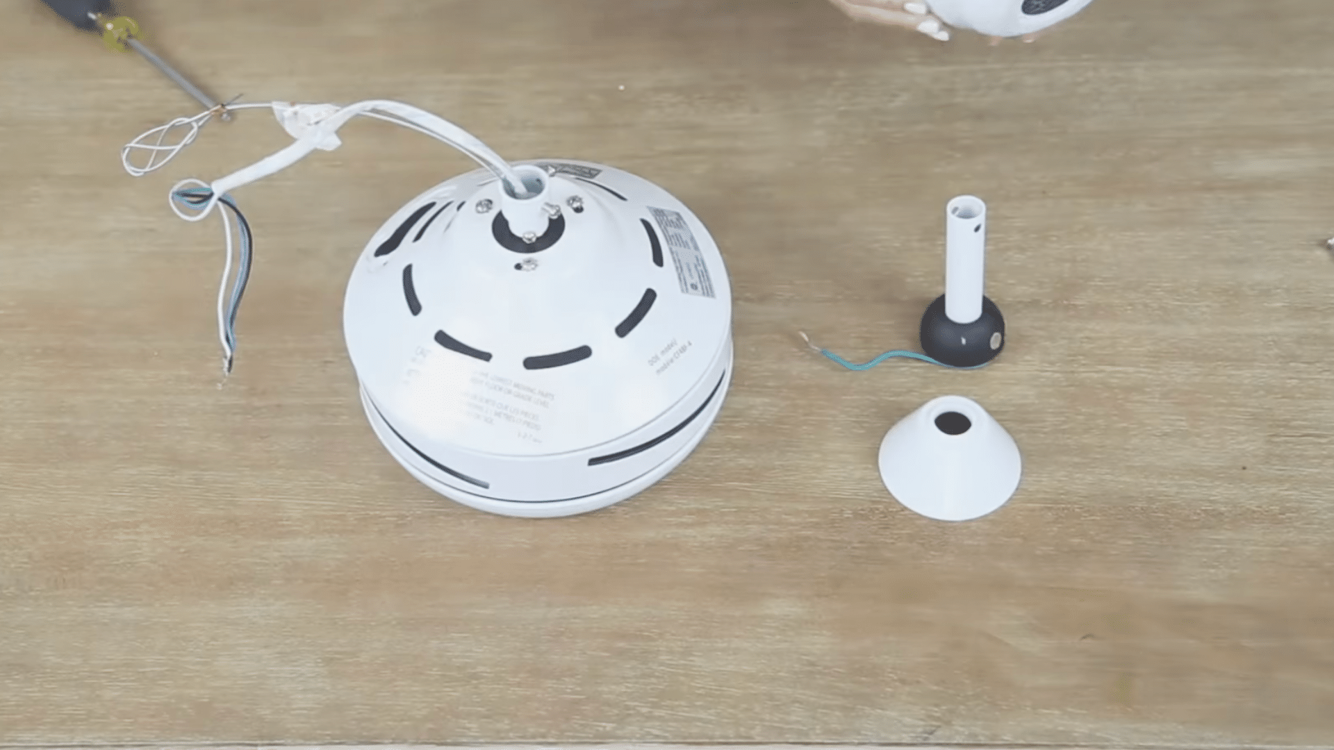 ceiling fan motor with exposed wires and detached mounting parts placed on a wooden workbench during repair