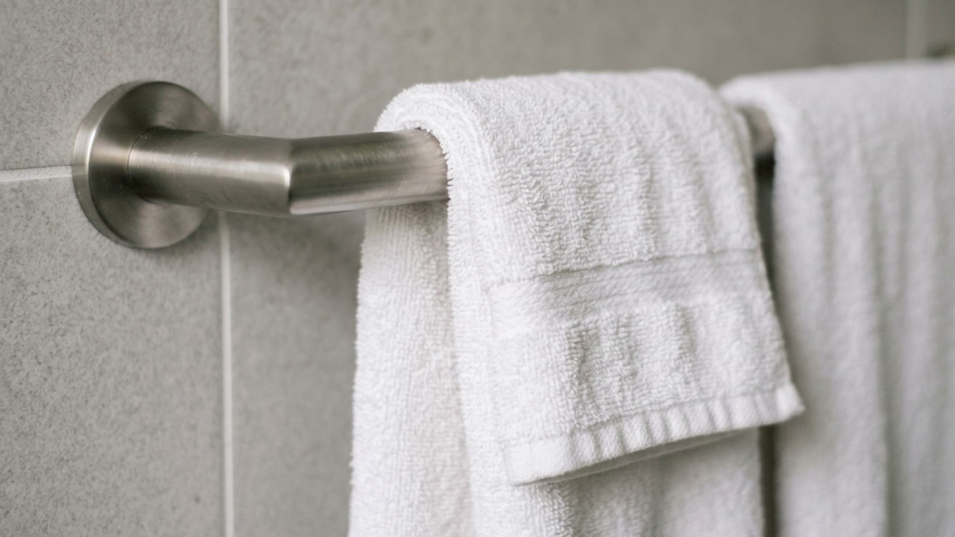 close up of a white towel folded over a brushed metal bar mounted on a light gray tiled bathroom wall