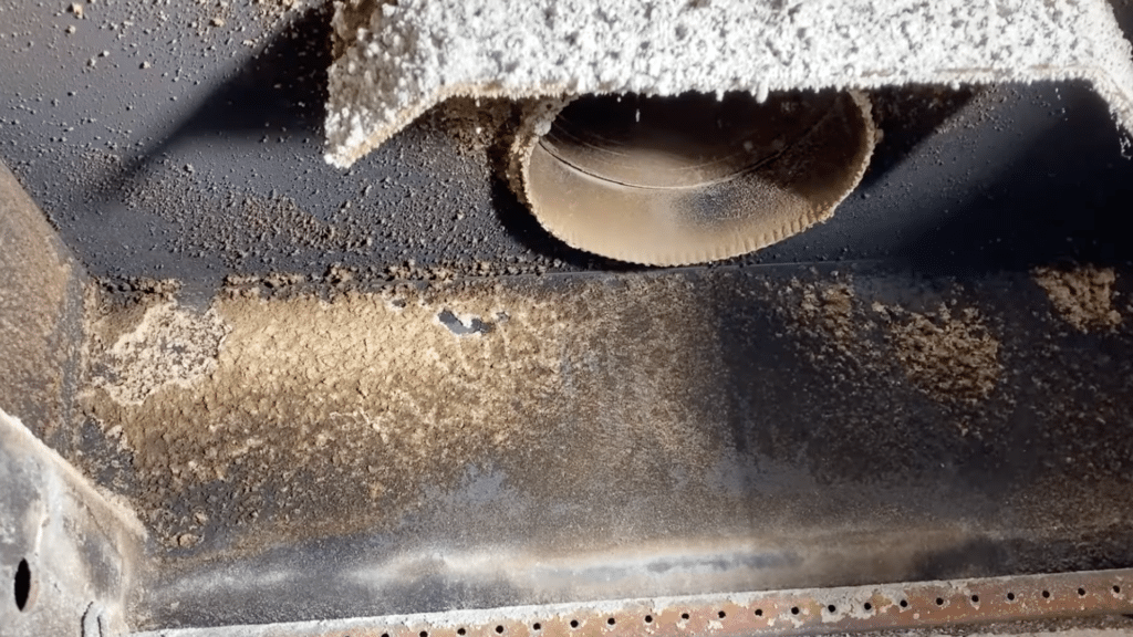 close up of dusty stove interior with ash buildup around round pipe and insulation panel above