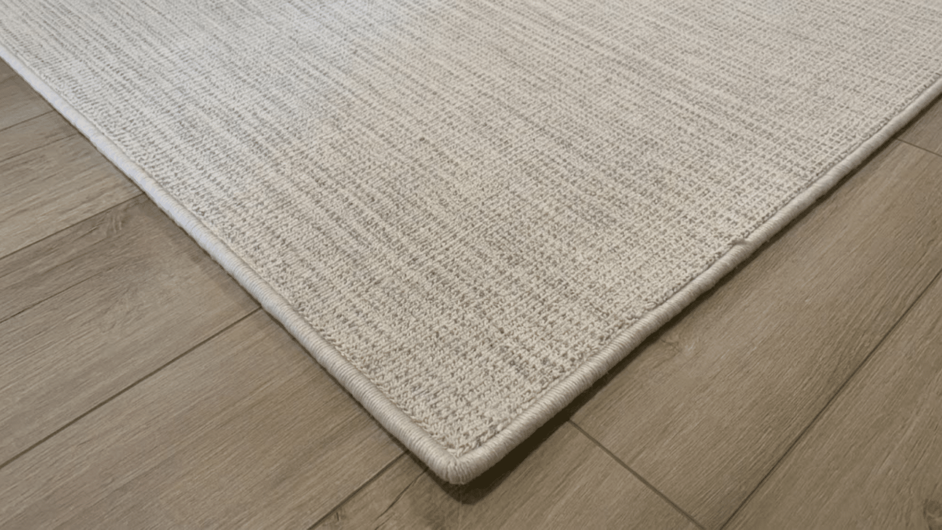 close up of neutral woven rug with stitched edges placed on wooden floor showing texture and finish